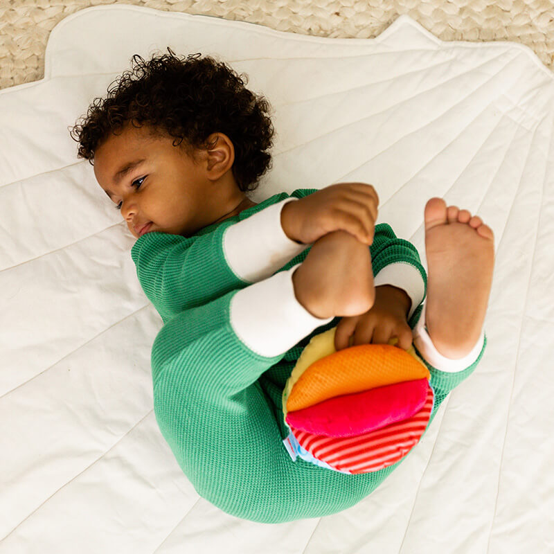 Baby playing with their feet holding HABA Rainbow Baby Ball